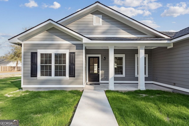 bungalow featuring a shingled roof, a front yard, and covered porch