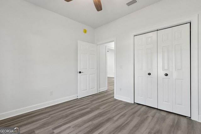 unfurnished bedroom featuring visible vents, baseboards, a closet, and wood finished floors