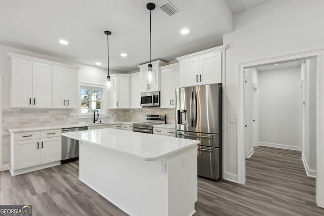kitchen featuring a sink, stainless steel appliances, white cabinetry, backsplash, and a center island