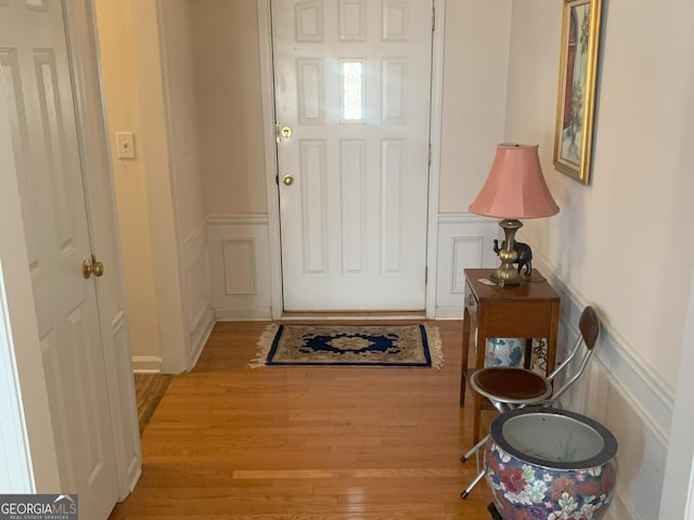 doorway to outside featuring light wood finished floors, wainscoting, and a decorative wall