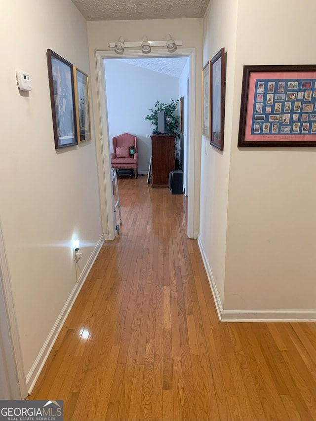 corridor with a textured ceiling, light wood-type flooring, and baseboards