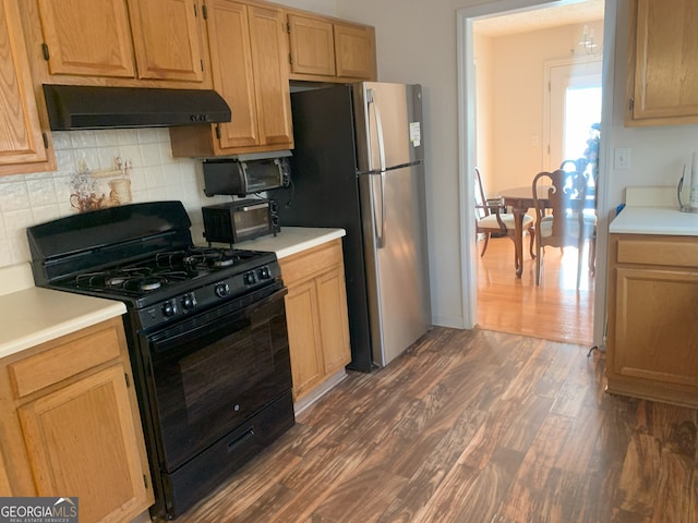 kitchen with dark wood-style floors, light countertops, black gas range oven, freestanding refrigerator, and under cabinet range hood