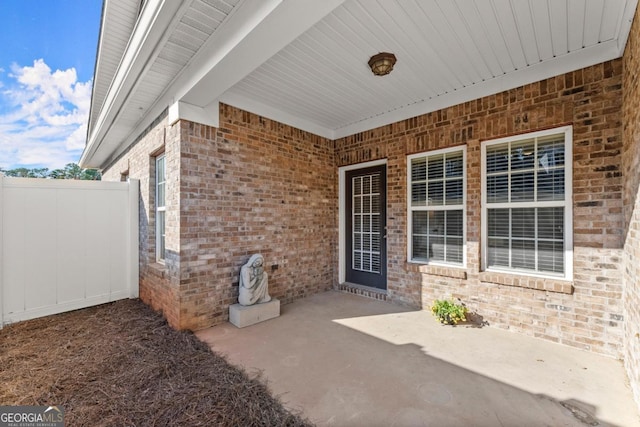 entrance to property featuring a patio, brick siding, and fence