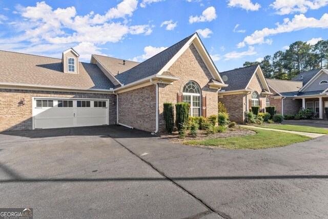 view of front of house with a garage, aphalt driveway, roof with shingles, and brick siding