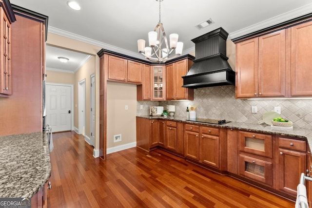 kitchen with visible vents, brown cabinetry, custom range hood, glass insert cabinets, and light stone counters