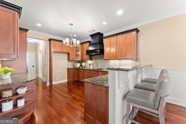 kitchen with dark stone counters, a peninsula, brown cabinetry, and custom exhaust hood