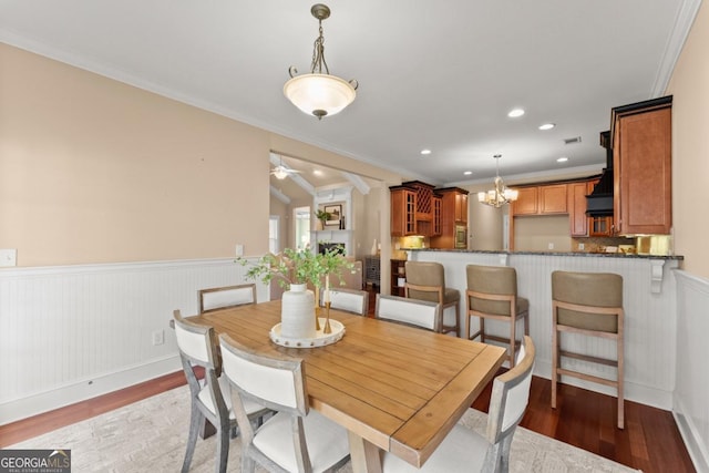 dining area featuring a wainscoted wall, crown molding, a fireplace, light wood finished floors, and ceiling fan