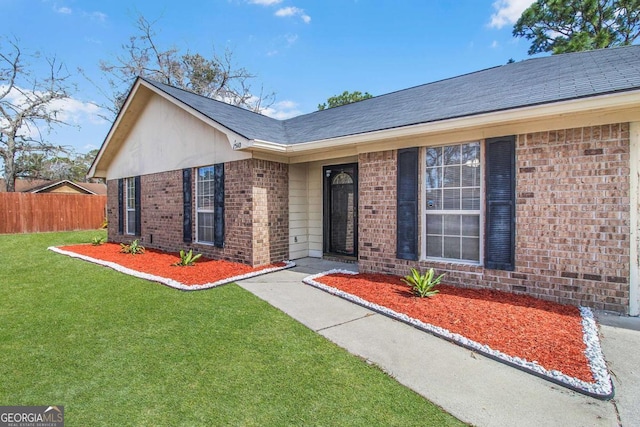 view of front of property featuring brick siding, a shingled roof, a front yard, and fence