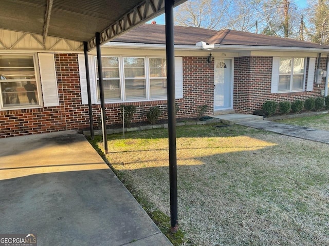 view of exterior entry featuring brick siding and a lawn