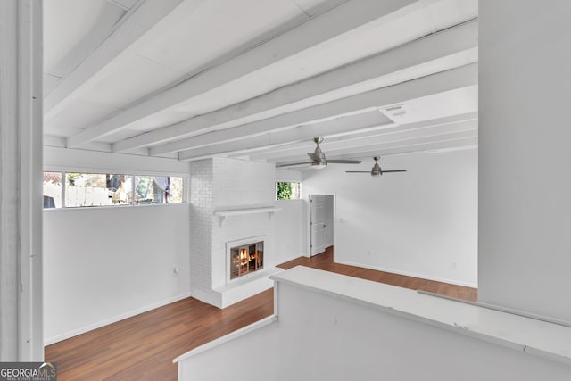 living area featuring ceiling fan, wood finished floors, baseboards, a brick fireplace, and beamed ceiling