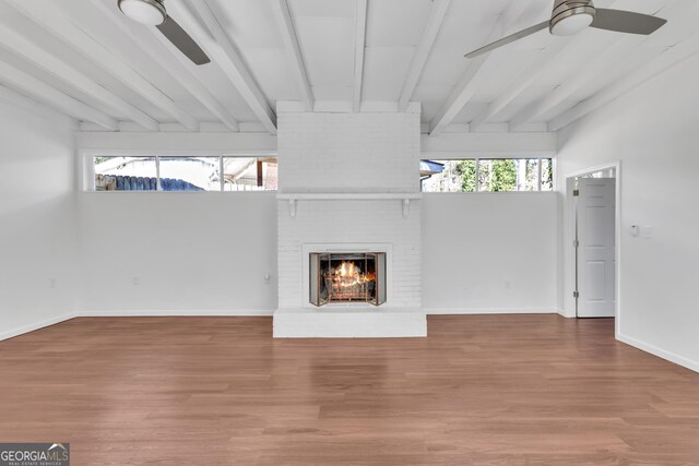 unfurnished living room featuring plenty of natural light, a fireplace, beam ceiling, and wood finished floors