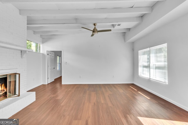 unfurnished living room featuring beamed ceiling, a brick fireplace, wood finished floors, and baseboards