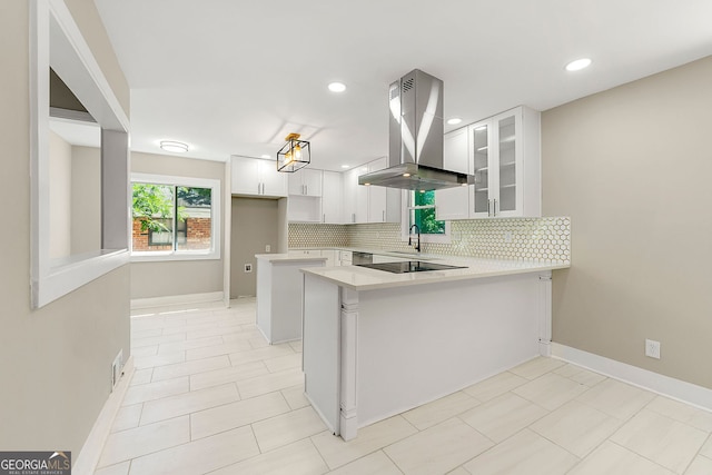 kitchen featuring a peninsula, tasteful backsplash, island range hood, and glass insert cabinets