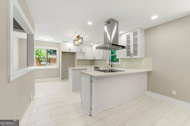 2682 Miriam Ln, Decatur, GA 30032 - kitchen featuring island range hood, a peninsula, backsplash, glass insert cabinets, and light countertops