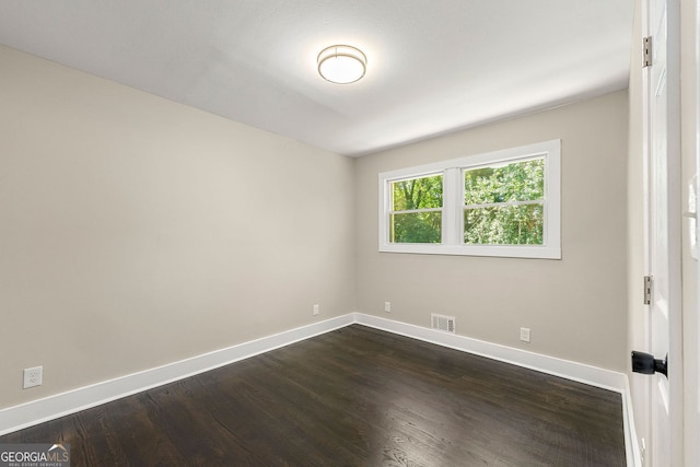 empty room with dark wood-style floors, visible vents, and baseboards