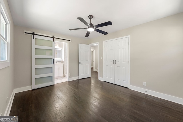 unfurnished bedroom with dark wood-style floors, a barn door, a closet, and baseboards