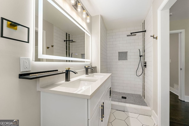 full bath featuring double vanity, visible vents, a tile shower, and a sink