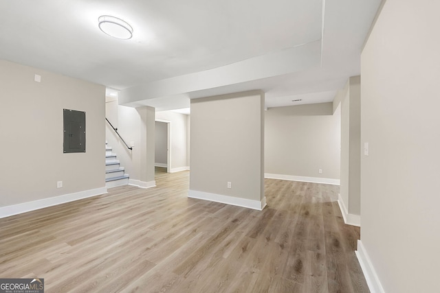 finished below grade area with baseboards, electric panel, stairway, and light wood finished floors