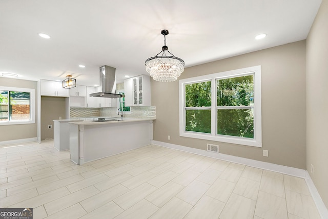 kitchen with a peninsula, visible vents, light countertops, tasteful backsplash, and island exhaust hood