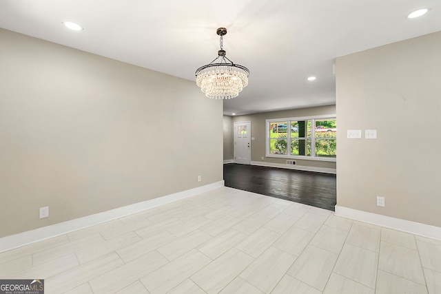 empty room with a chandelier, light wood finished floors, recessed lighting, and baseboards