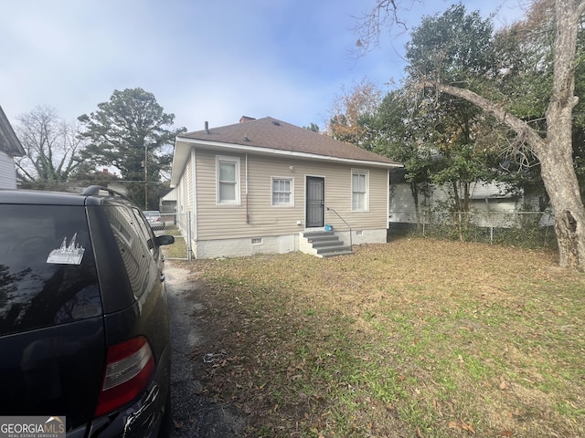 back of property featuring entry steps, fence, roof with shingles, crawl space, and a lawn