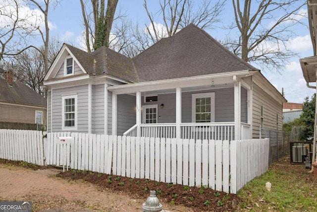 view of front of property with central AC unit, covered porch, fence, and roof with shingles