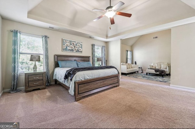 carpeted bedroom with a tray ceiling, multiple windows, visible vents, and baseboards