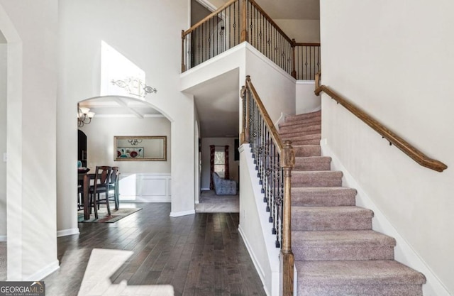 staircase with baseboards, a high ceiling, arched walkways, and wood finished floors