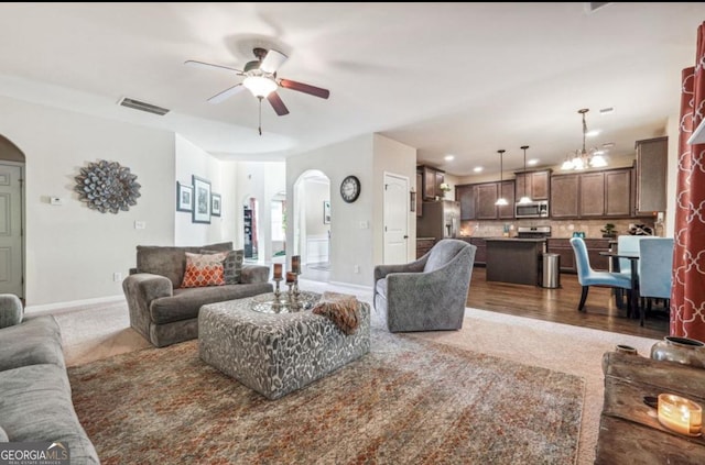 living room with visible vents, arched walkways, baseboards, and ceiling fan with notable chandelier