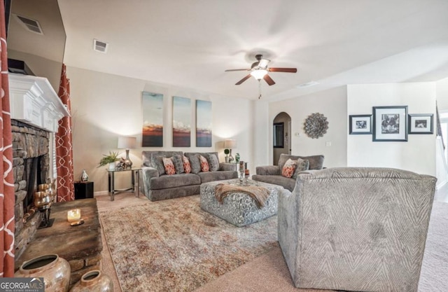 living area featuring a ceiling fan, arched walkways, visible vents, and a stone fireplace