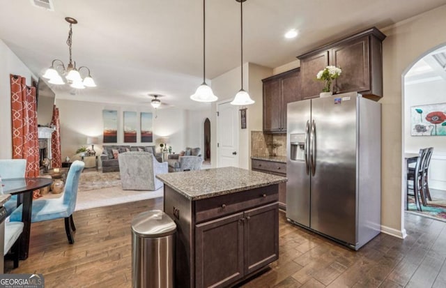 kitchen featuring arched walkways, dark wood finished floors, a fireplace, stainless steel refrigerator with ice dispenser, and dark brown cabinetry