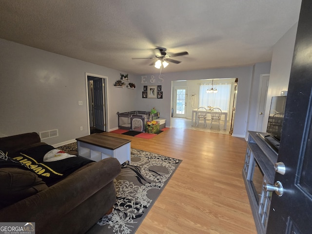 living room with light wood finished floors, baseboards, visible vents, and a textured ceiling