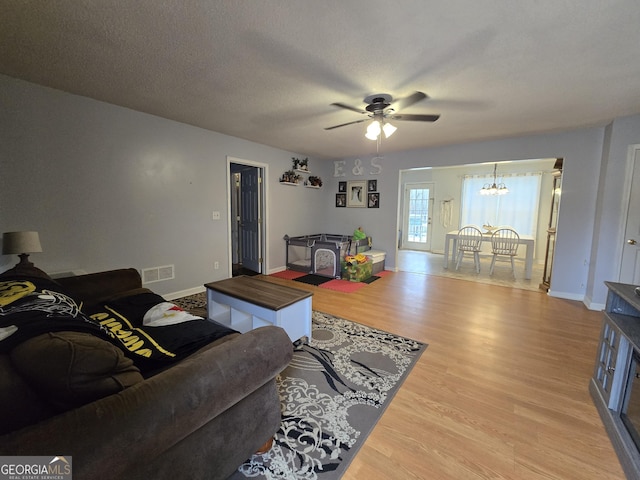 220 Joe Dr, Temple, GA 30179 - living room featuring a textured ceiling, light wood-style flooring, visible vents, baseboards, and ceiling fan with notable chandelier