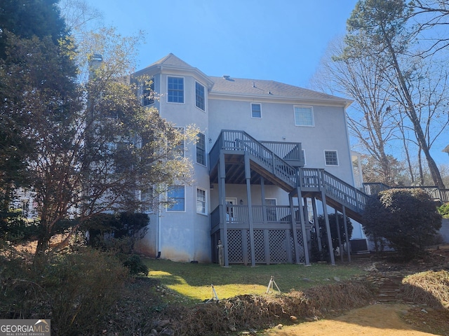 rear view of house featuring a yard, stairway, and stucco siding