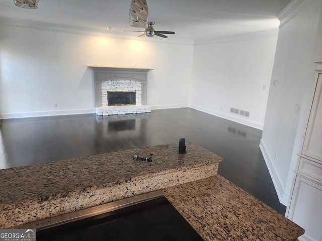 unfurnished living room with a fireplace, visible vents, baseboards, a ceiling fan, and ornamental molding