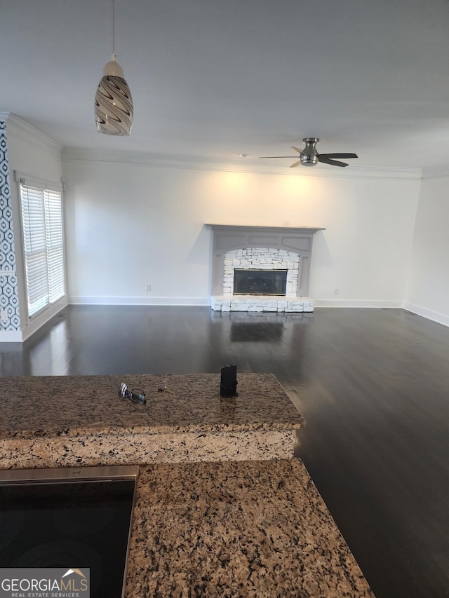 kitchen with baseboards, a ceiling fan, dark wood-style floors, ornamental molding, and a stone fireplace