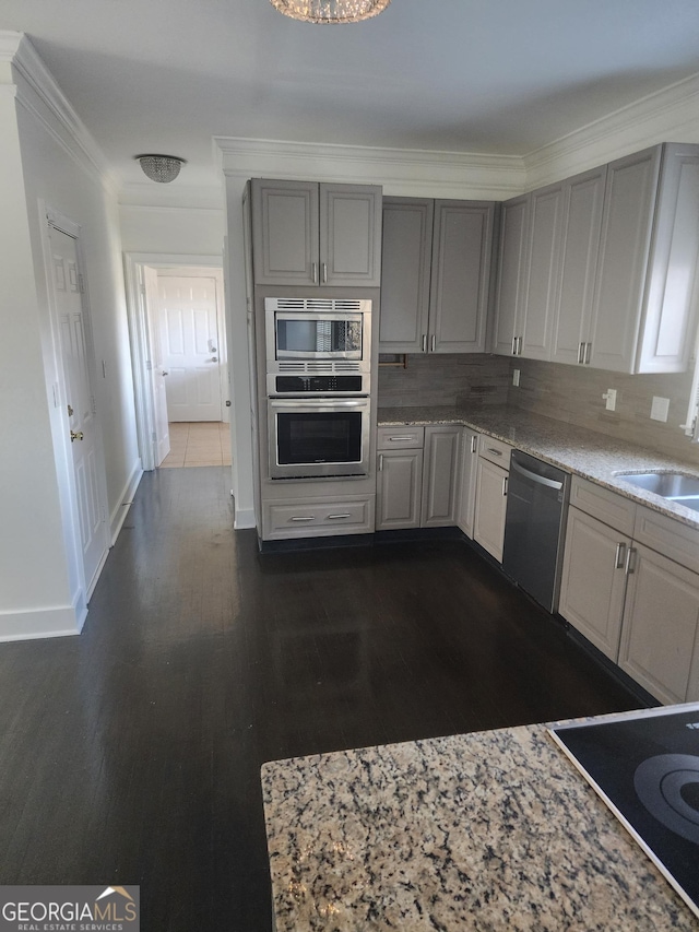 kitchen featuring crown molding, stainless steel appliances, tasteful backsplash, gray cabinets, and a sink