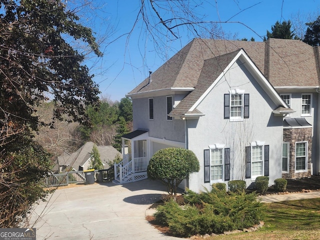 view of front of property featuring fence, driveway, stone siding, roof with shingles, and stucco siding