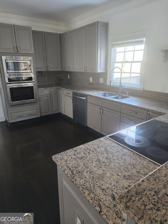 kitchen with light stone counters, ornamental molding, gray cabinets, stainless steel appliances, and a sink