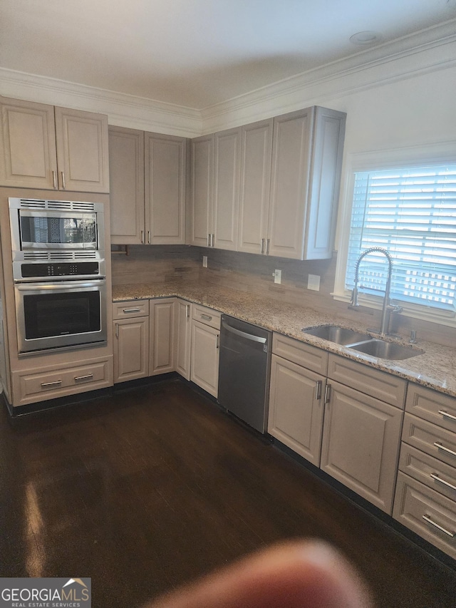 kitchen with light stone counters, dark wood-style floors, crown molding, appliances with stainless steel finishes, and a sink