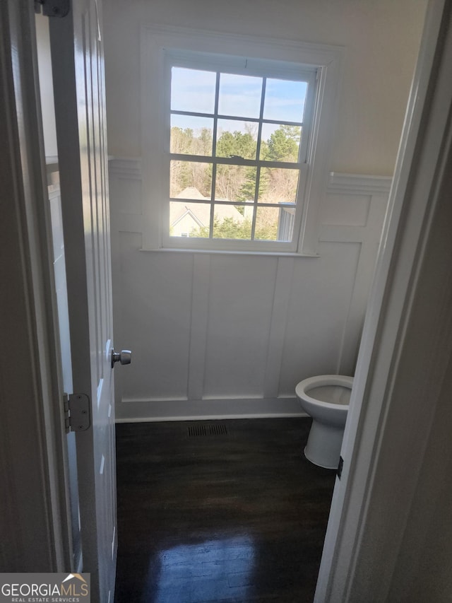 bathroom with visible vents, a decorative wall, toilet, wainscoting, and wood finished floors