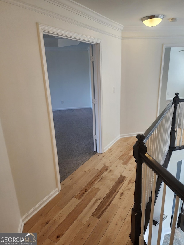 hallway featuring light wood-type flooring, ornamental molding, and an upstairs landing