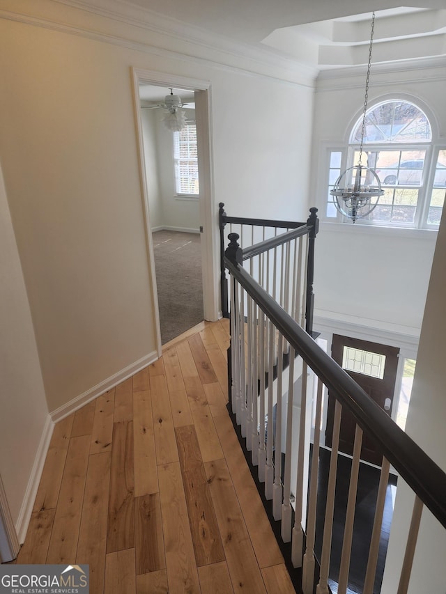 hall with crown molding, a notable chandelier, light wood-style flooring, an upstairs landing, and baseboards