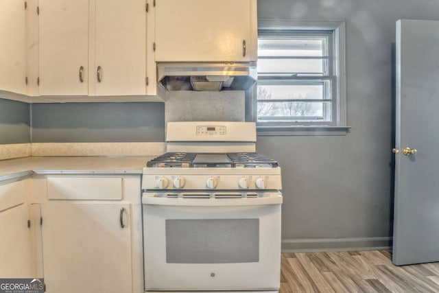 kitchen featuring white gas stove, light countertops, light wood-style floors, baseboards, and exhaust hood