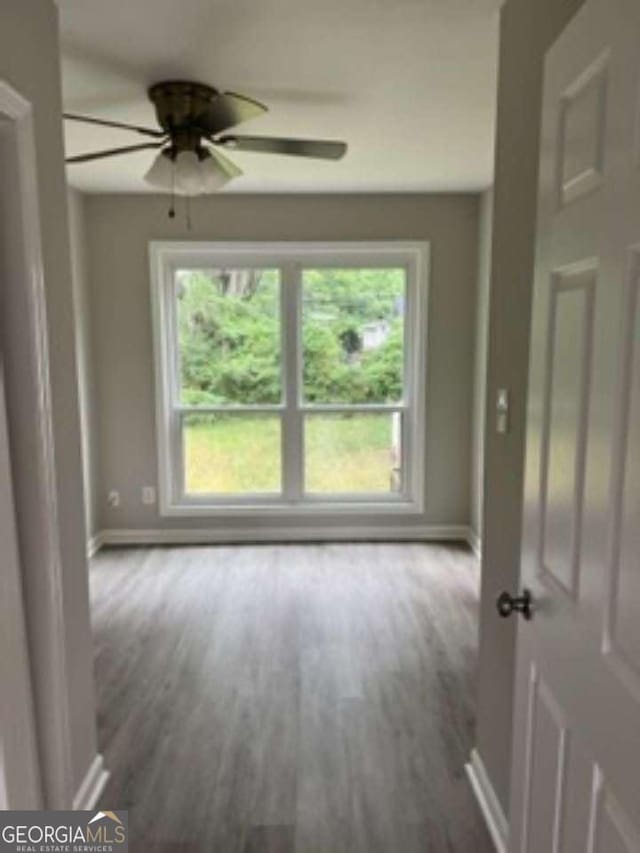 empty room featuring wood finished floors, a ceiling fan, and baseboards