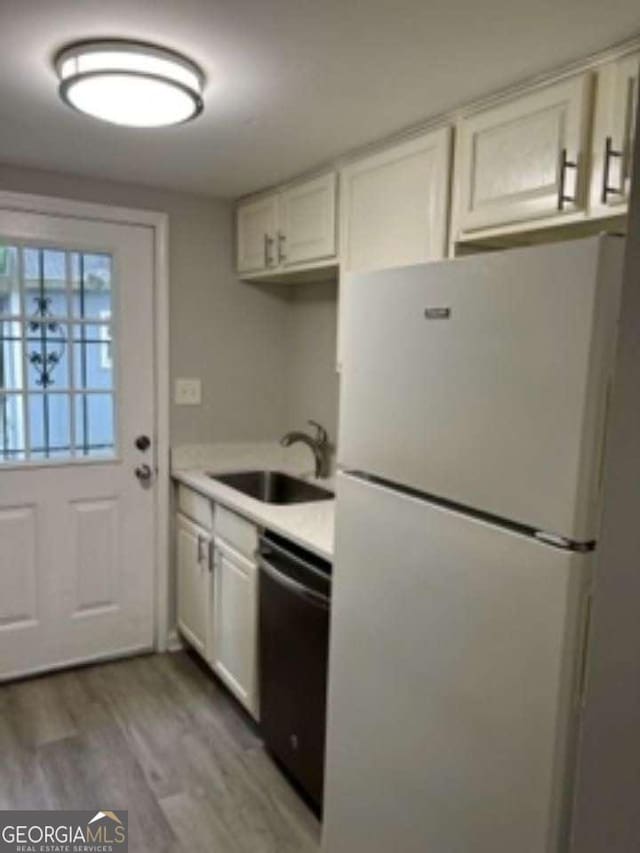 kitchen featuring light countertops, freestanding refrigerator, white cabinets, a sink, and dishwasher