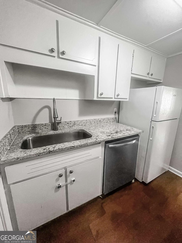 kitchen with light stone counters, freestanding refrigerator, stainless steel dishwasher, white cabinetry, and a sink