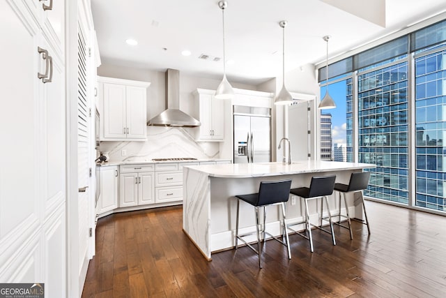 kitchen featuring visible vents, backsplash, wall chimney range hood, a wall of windows, and built in fridge