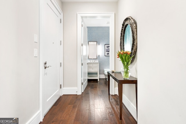 hall with wallpapered walls, dark wood-type flooring, and baseboards