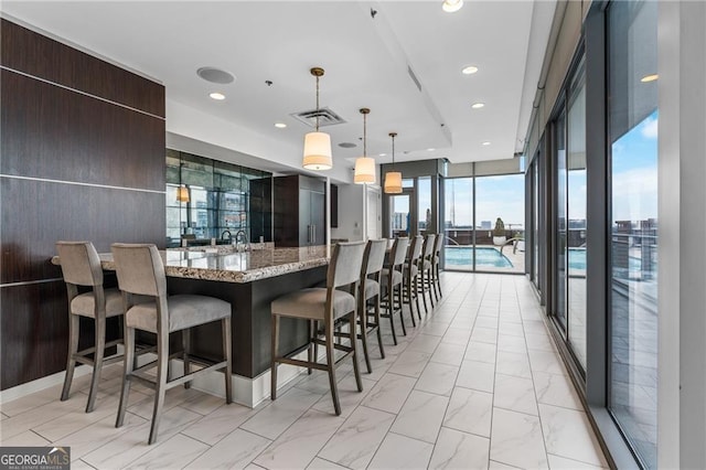 kitchen featuring light stone countertops, visible vents, a kitchen breakfast bar, modern cabinets, and marble finish floor